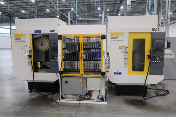 Two industrial FANUC CNC machines with control panels, yellow accents, and interconnecting equipment in a spacious facility.